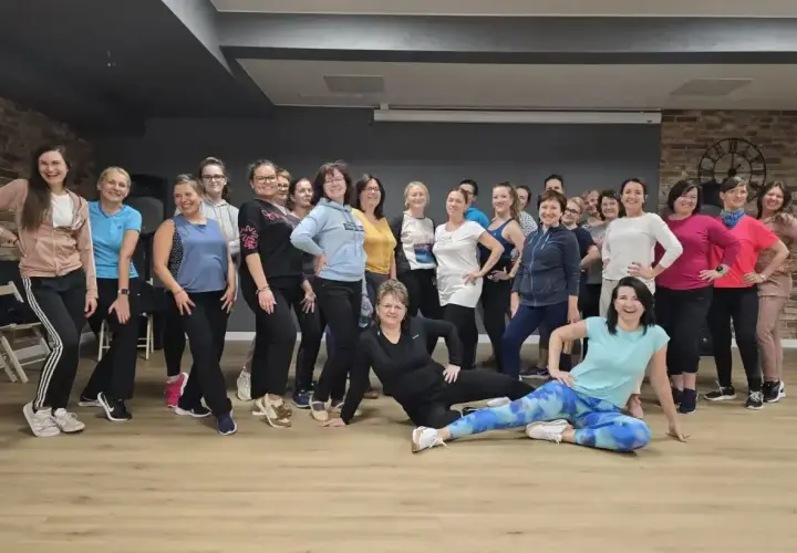 Grupa kobiet na zajęciach nauka tańca, uśmiechnięte, w sportowych strojach, pozują do zdjęcia.
