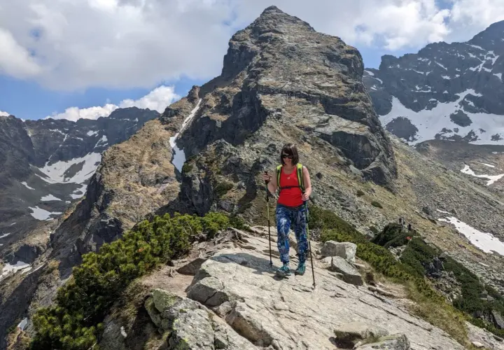 Kobieta z kijkami trekkingowymi na skalistej ścieżce w Dolinie Gąsienicowej. W tle majestatyczny szczyt i ośnieżone zbocza.