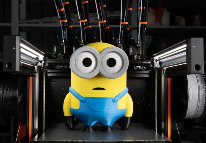 Minion wydrukowany na dobra drukarka 3d. Maszyna z wieloma głowicami i szpulami filamentu w tle.