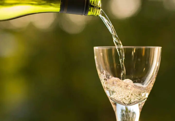 Un vin blanc pétillant est versé dans un verre, créant une mousse légère qui rappelle le sucre dans le vin.
