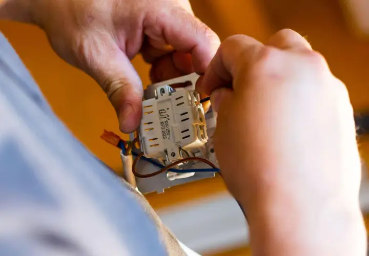 Ręce elektryka podłączają przewody do mechanizmu gniazdka. To kluczowy etap prac, wpływający na koszt instalacji elektrycznej.