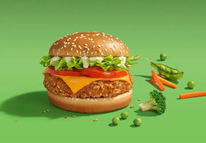 Pyszny wege burger McDonald's z chrupiącym kotletem, serem, pomidorem i sałatą. Obok świeże warzywa: groszek, marchewka i brokuł.