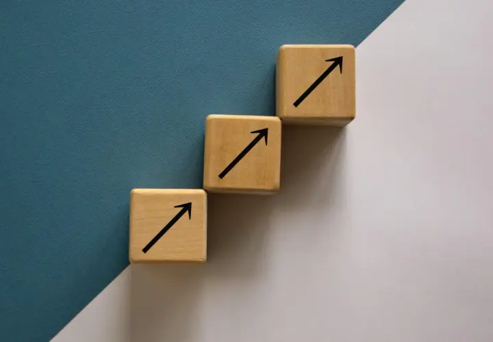 Trzy drewniane kostki tworzą schody, każda z czarną strzałką w górę. To symboliczne ten square games akcje, które rosną.