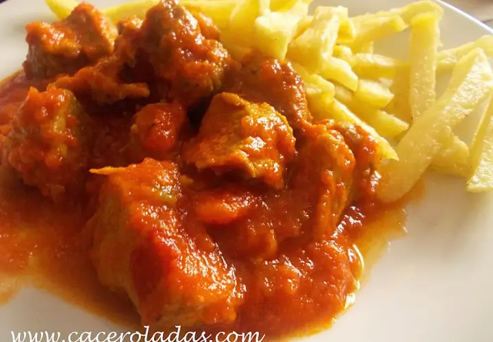 Sabroso carne de cerdo con tomate de la abuela, jugoso y tierno, acompañado de patatas fritas crujientes.