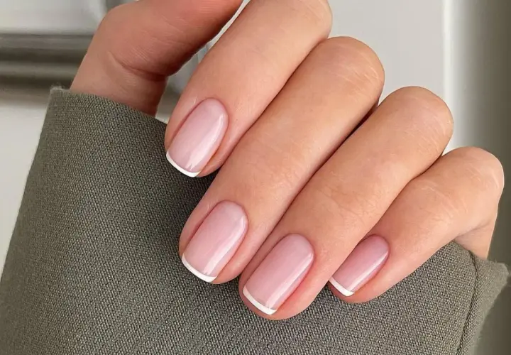 Dłoń z idealnie wykonanymi, eleganckimi paznokciami french. Delikatny róż i klasyczna biel tworzą ponadczasowy manicure.