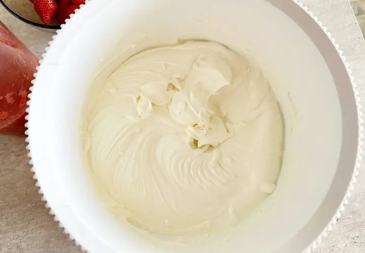 Gładki, puszysty krem z mascarpone w białej misie, gotowy do deseru. Obok miski widać truskawki.