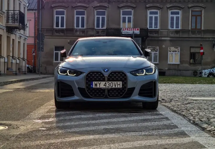 Szare BMW 420i z charakterystycznym grillem stoi na przejściu dla pieszych. W tle kamienice.