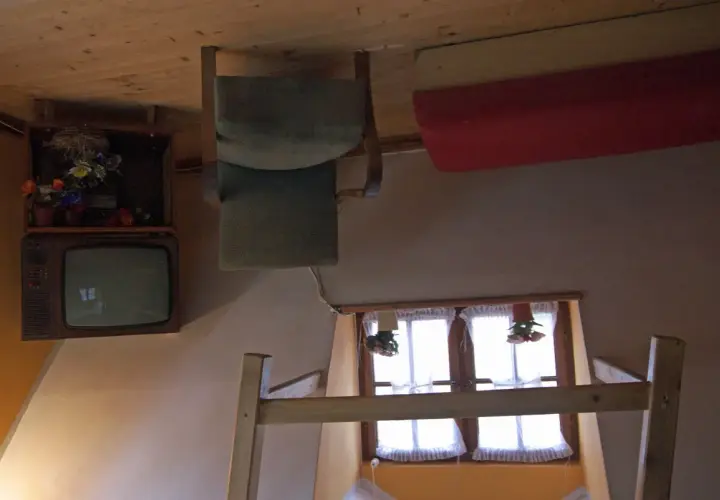 Wnętrze domu do góry nogami w Szymbarku: odwrócony telewizor, krzesło i łóżko.