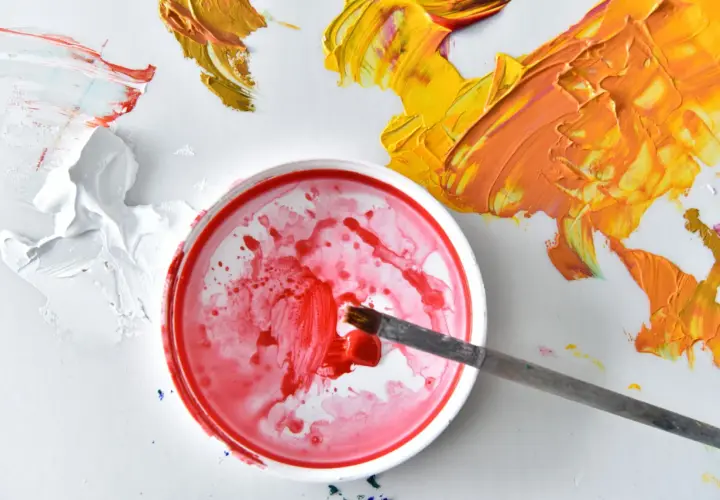 Pennello intinge nel rosso per capire come miscelare i colori per pittura murale. Macchie di giallo e arancio vibrante completano la scena.