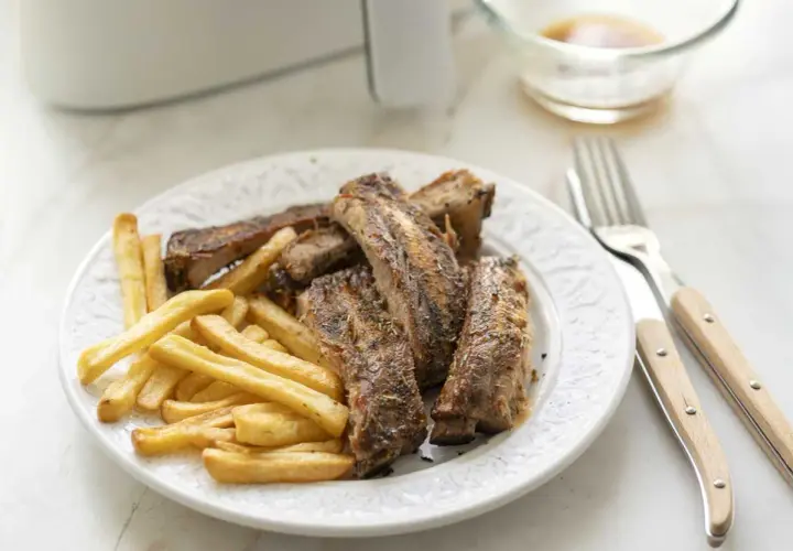 Costillas jugosas y patatas fritas crujientes, recién salidas de la freidora de aire. Un plato perfecto para disfrutar.