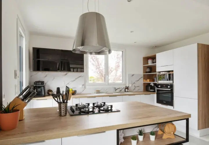 Cuisine moderne avec îlot central en bois, hotte design en alliage inox, et électroménagers intégrés.