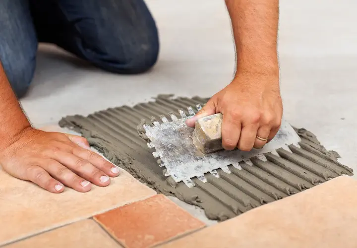 Mani esperte stendono la colla per piastrelle con una spatola dentata, creando un letto uniforme. La quantità di colla per piastrelle al mq è fondamentale per una posa perfetta.