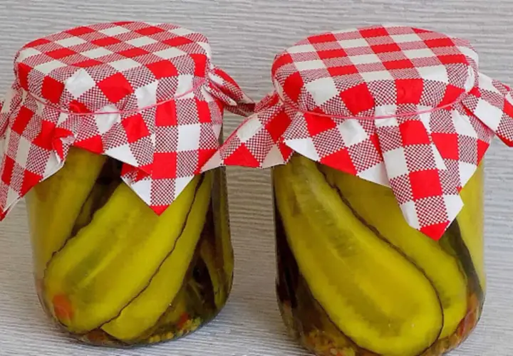 Słoiki z ogórkami w curry ze skórką, ozdobione czerwono-białymi kratkowanymi chusteczkami.