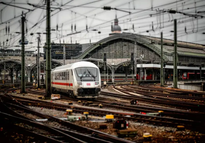 Pociąg DB na stacji, skomplikowana sieć torów i trakcji elektrycznej. Widoczna blokada liniowa sygnalizuje gotowość do odjazdu.
