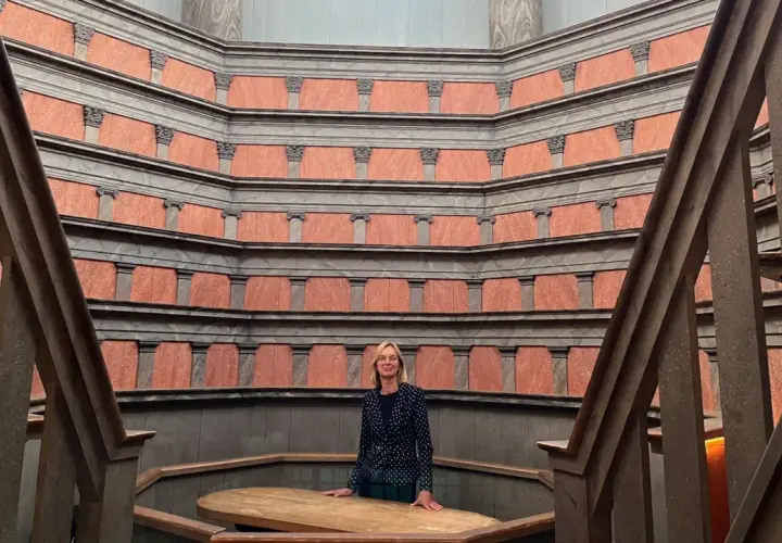 En kvinna står i den imponerande **anatomiska teatern Uppsala**. De rödbruna väggarna med sina pelare skapar en unik atmosfär.