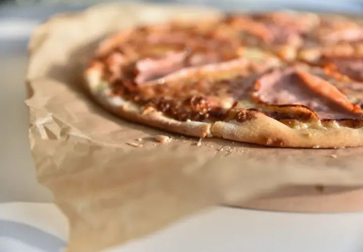 Zbliżenie na pizzę z szynką na papierze do pieczenia.