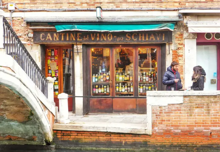 Cantina del Vino, un posto ideale per mangiare a Venezia spendendo poco. Coppia parla davanti al locale pieno di bottiglie.