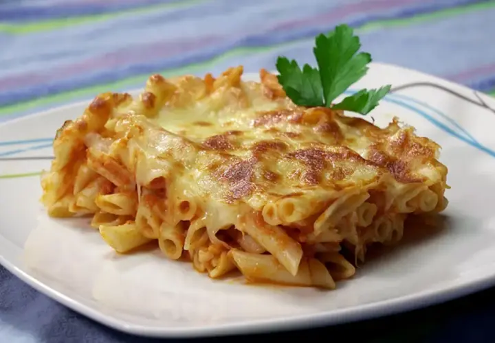 Porción de macarrones al horno gratinados con queso derretido y una hoja de perejil, servida en un plato blanco.