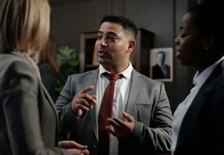 Un homme en costume explique avec passion à deux femmes, peut-être une affaire où ils risquent d'être déboutés en justice.