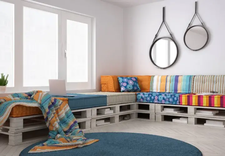 Divano con pallet, colorato e accogliente, con cuscini vivaci e una coperta morbida. Perfetto per un angolo relax.