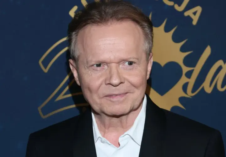 Michał Bajor w czarnym garniturze i białej koszuli, uśmiecha się. W tle złote napisy i serce.