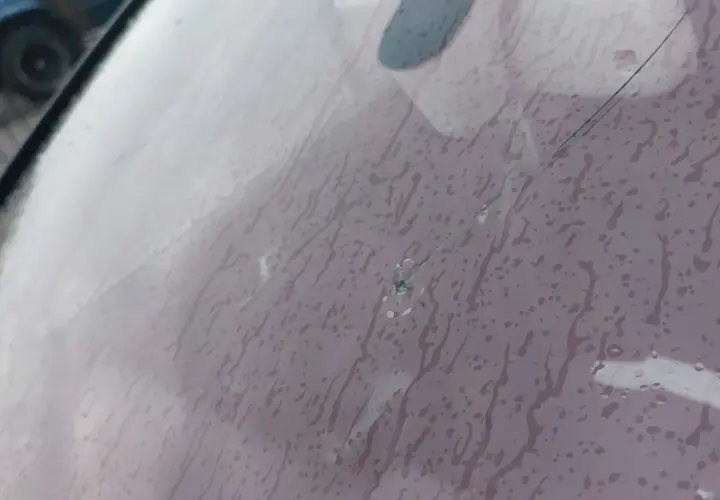 Pęknięta szyba w aucie z widocznym punktowym uszkodzeniem i pajęczyną pęknięć. Krople deszczu spływają po powierzchni.