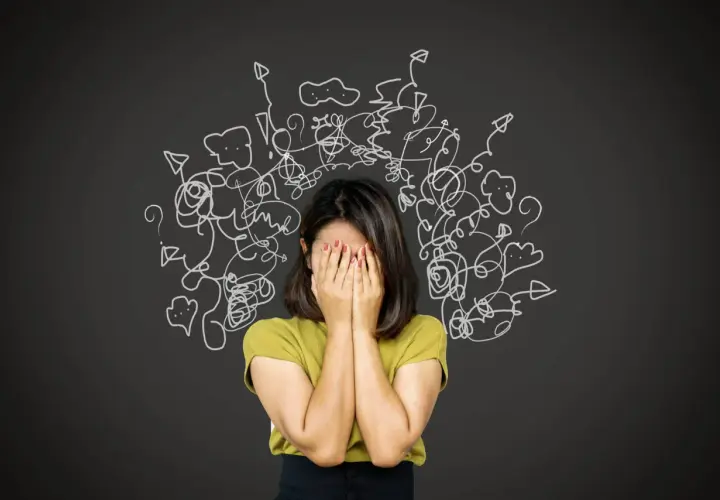 Donna con le mani sul viso, circondata da disegni caotici. Un'immagine che evoca la difficoltà nel come trattare un paranoico, con pensieri confusi e ansia.