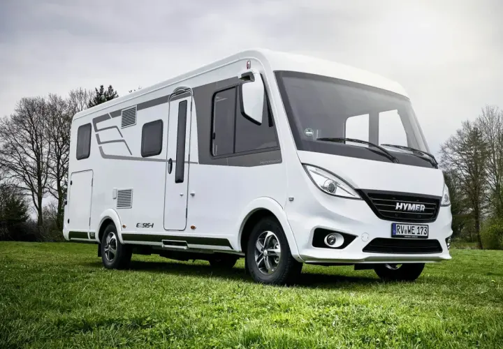Biała kamper z serii Hymermobil, produkt Erwin Hymer Group, stoi na zielonej trawie.