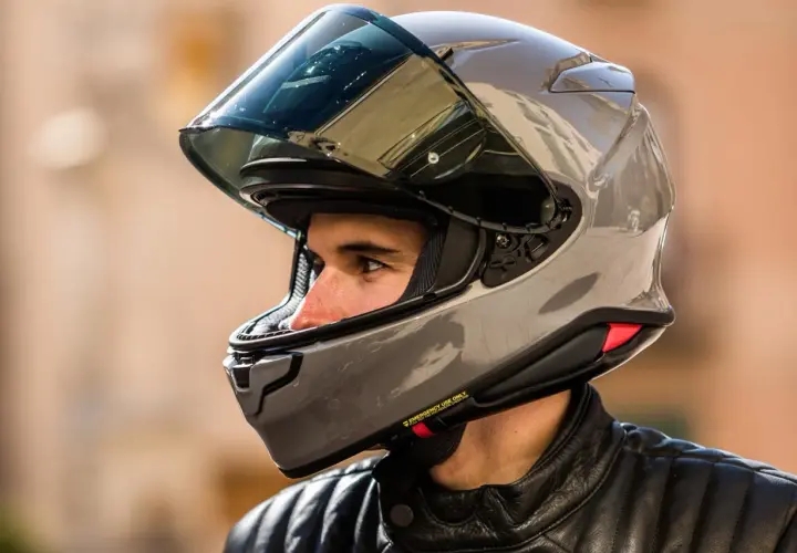 Hombre con casco moto 125 gris brillante, visor oscuro y chaqueta de cuero negra.