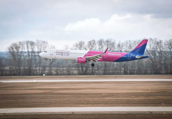 Samolot Wizz Air z różowym i niebieskim ogonem ląduje na pasie startowym.