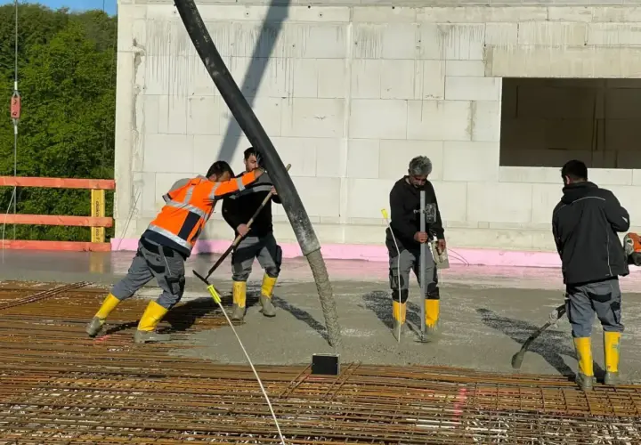 Arbeiter gießen Beton für die Bodenplatte. Sie schalen die Platte aus und verteilen den frischen Beton mit Werkzeugen.