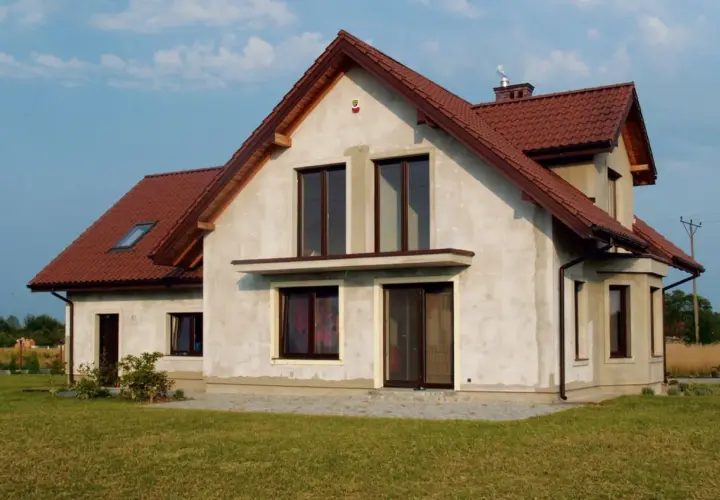 Dom w budowie z brązowym dachem, w tle linia wysokiego napięcia.