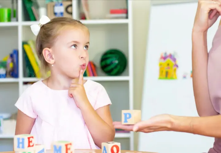 Dziewczynka z palcem przy ustach myśli podczas zabawy edukacyjnej z literkami.