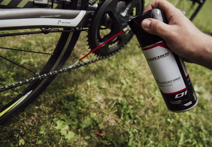 Dłoń trzyma puszkę z odtłuszczaczem do rowerów, aplikując go na łańcuch. Czy benzyna ekstrakcyjna odtłuszcza? Ten spray na pewno tak!