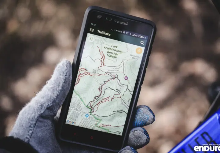 Rękawiczka trzyma smartfon z mapą szlaków rowerowych w Beskidzie Małym. To darmowa aplikacja do jazdy na rowerze, idealna na wyprawę.