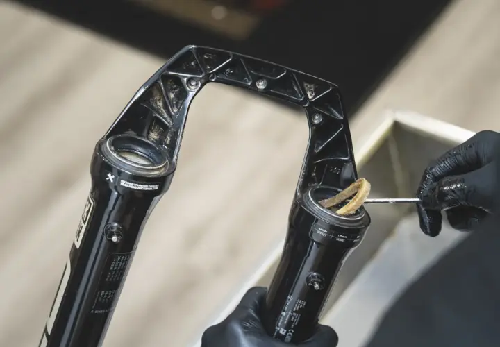 Gloved hands clean a RockShox Revelation RC fork, removing dirt from the stanchions.
