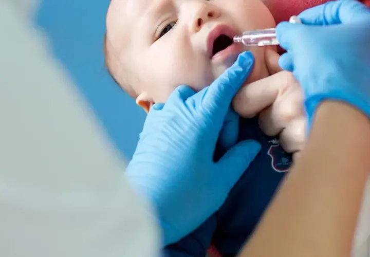 Ein Baby erhält Tropfen zur Vorbeugung von Rotavirus-Symptomen. Blaue Handschuhe schützen die Hände des Arztes.