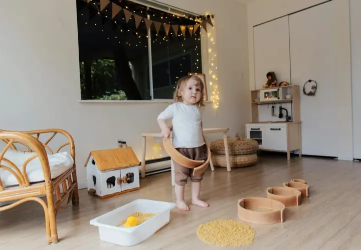 Dziecko bawi się w pokoju inspirowanym 10 zasadami Montessori. Drewniane zabawki, domek i kuchnia zachęcają do samodzielnej nauki.