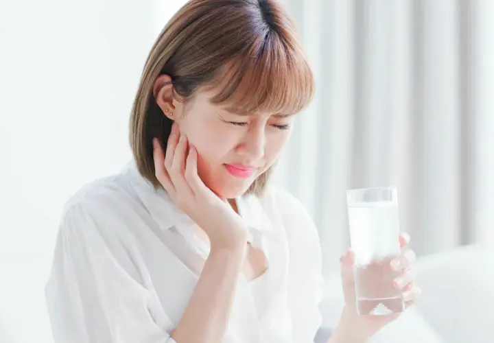 Donna con espressione sofferente, tiene un bicchiere d'acqua, soffre di ipersensibilità dentale.
