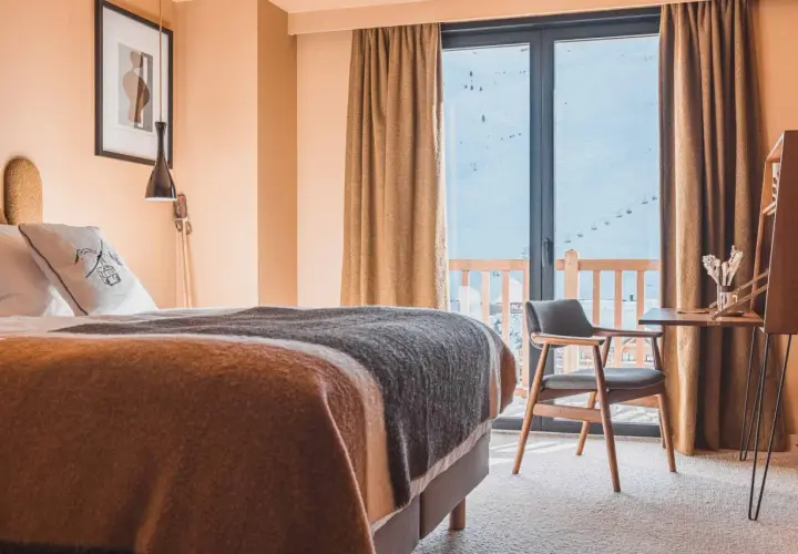 Chambre d'hôtel avec lit douillet, vue sur les montagnes enneigées et télécabines.