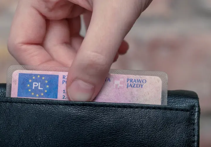 Dłoń wkłada do czarnego portfela polskie prawo jazdy. Widoczny jest numer blankietu prawa jazdy.