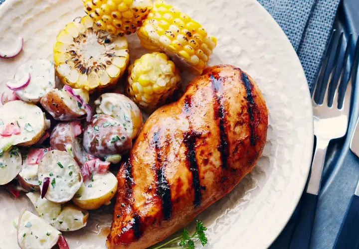 Un délicieux poulet grillé au sirop d'érable, servi avec une salade de pommes de terre crémeuse et des épis de maïs rôtis.