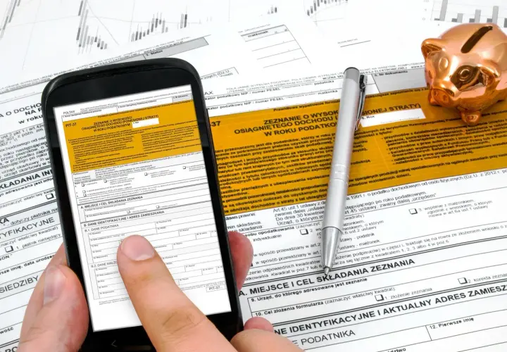 Smartfon z formularzem PIT-37 i złotą świnką skarbonką. Instrukcja jak rozliczyć PIT 37.