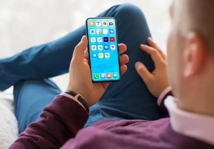 Dłoń trzyma smartfon z ikonami aplikacji. Szybkość ładowania telefonu zależy od wielu czynników, np. ładowarki i stanu baterii.