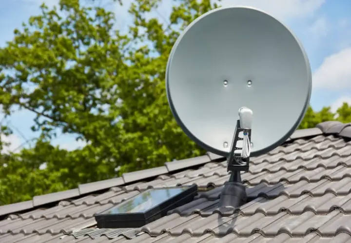 Antena satelitarna na dachu, obok okna dachowego. Prawidłowe ustawienie to klucz do tego, jak poprawić jakość sygnału satelitarnego.