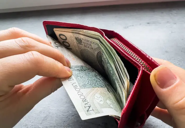 Ręce wkładają pieniądze do czerwonego portfela. To może być symbol wsparcia finansowego, jak zus renta rodzinna po mężu.