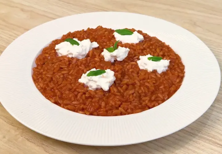 Un invitante risotto al pomodoro, arricchito da ciuffi di ricotta fresca e basilico, pronto per essere gustato.