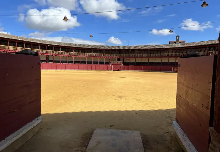 La plaza de toros de Toro, con su arena dorada y gradas rojas, espera bajo un cielo azul con nubes.