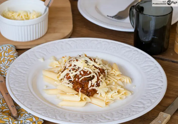 Macarrones con carne picada, cubiertos de queso rallado, servidos en un plato blanco con un diseño floral.