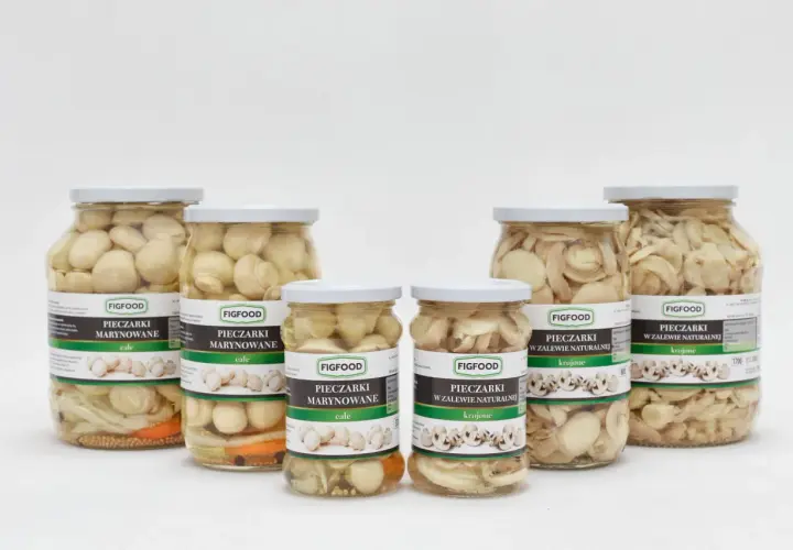 Sześć słoików z marynowanymi pieczarkami Figfood, w tym całe i krojone, na białym tle.